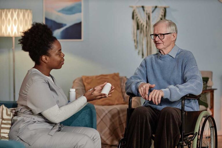 Caregiver helps an older resident safely walk through a bright assisted living hallway.